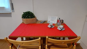 A small dining area with a red tablecloth, two wooden chairs, a basket with green plants, a sign about disinfection and sanitization, and a coffee machine. - Bnbook-Ughelli Rho Studio (Rho)
