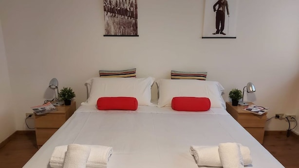 A double bed with white and red bedding, two nightstands with lamps, and two framed pictures on the wall. - Bnbook-Ughelli Rho Studio (Rho)
