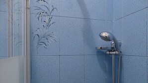 A bathroom with blue speckled tiles, a shower with a handheld showerhead, and a visible towel rack. - Bnbook-Ughelli Rho Studio (Rho)