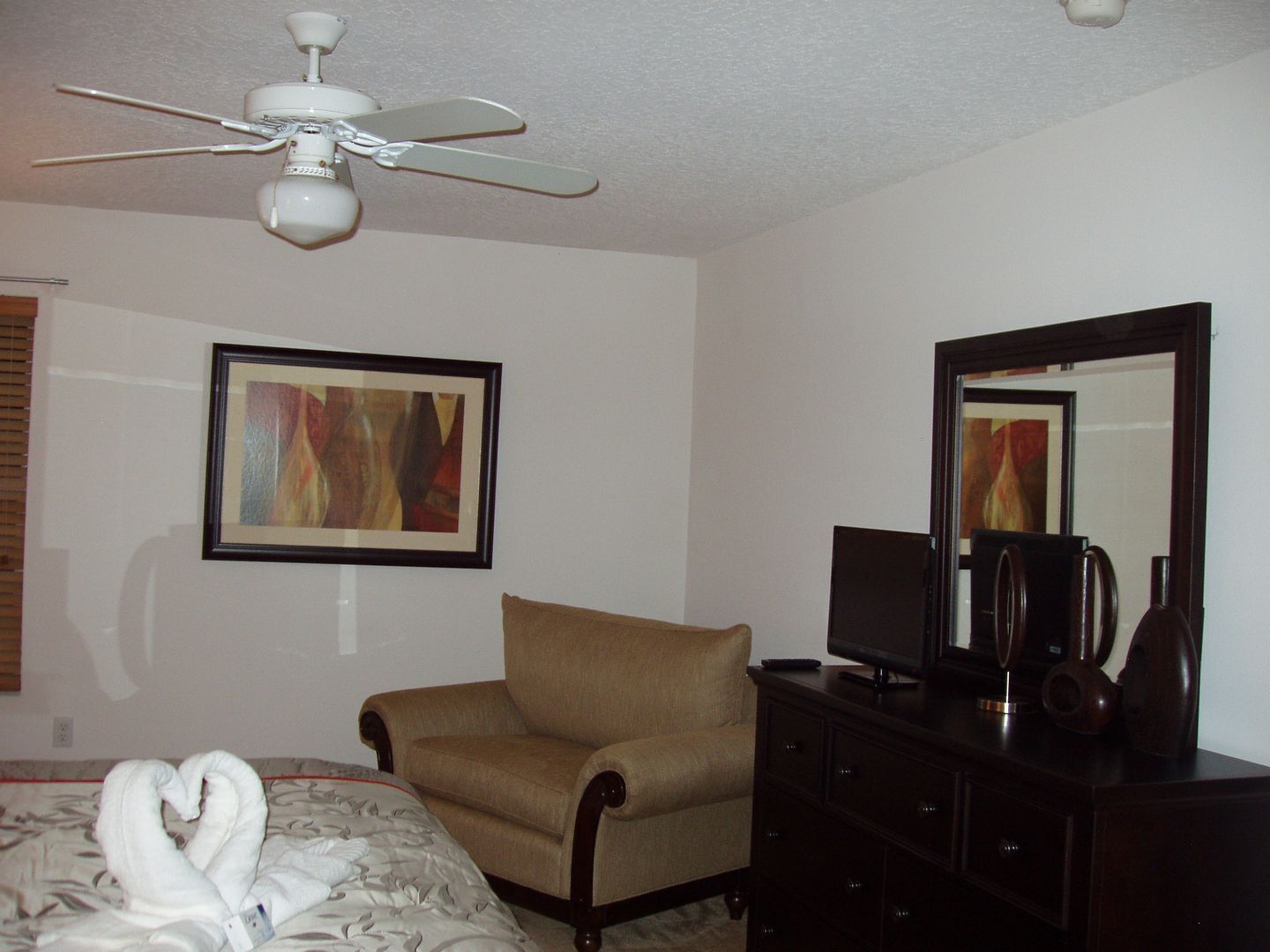 A hotel room with a bed, a chair, a dresser, a television, and a ceiling fan.