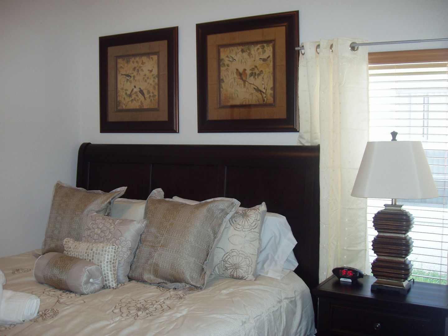 Una cama bien hecha con almohadones estampados, un cabecero oscuro y dos cuadros en la pared.