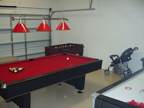 Ett biljardbord med rött ljus, ett fotbollsspel och en barnvagn i ett rum med vita väggar och en garageport.