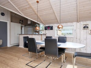 Een moderne keuken met houten wanden, een eethoek met een ronde tafel en zwarte stoelen, en hanglampen.