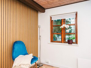 Une pièce avec une chaise bleue, un mur lambrissé en bois, une fenêtre donnant sur un paysage verdoyant et un lampadaire.