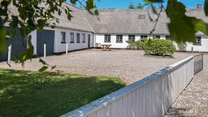 A building with a gravel courtyard, a wooden fence, and a small table. - 14 Person Holiday Home in Orsted (Ørsted)