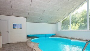 An indoor swimming pool with a curved edge, a tiled floor, a bench along the wall, and a window providing natural light. - 14 Person Holiday Home in Orsted (Ørsted)