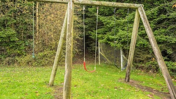 A wooden swing set in a grassy area with dense trees in the background.