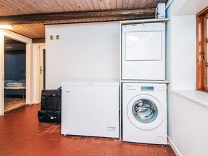 A laundry area with a washing machine and dryer stacked against a wall, a door leading to a bedroom, and a wooden ceiling. - 14 Person Holiday Home in Orsted (Ørsted)
