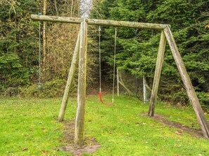 Une balançoire en bois installée dans un espace herbeux, avec des arbres à feuilles denses en arrière-plan.