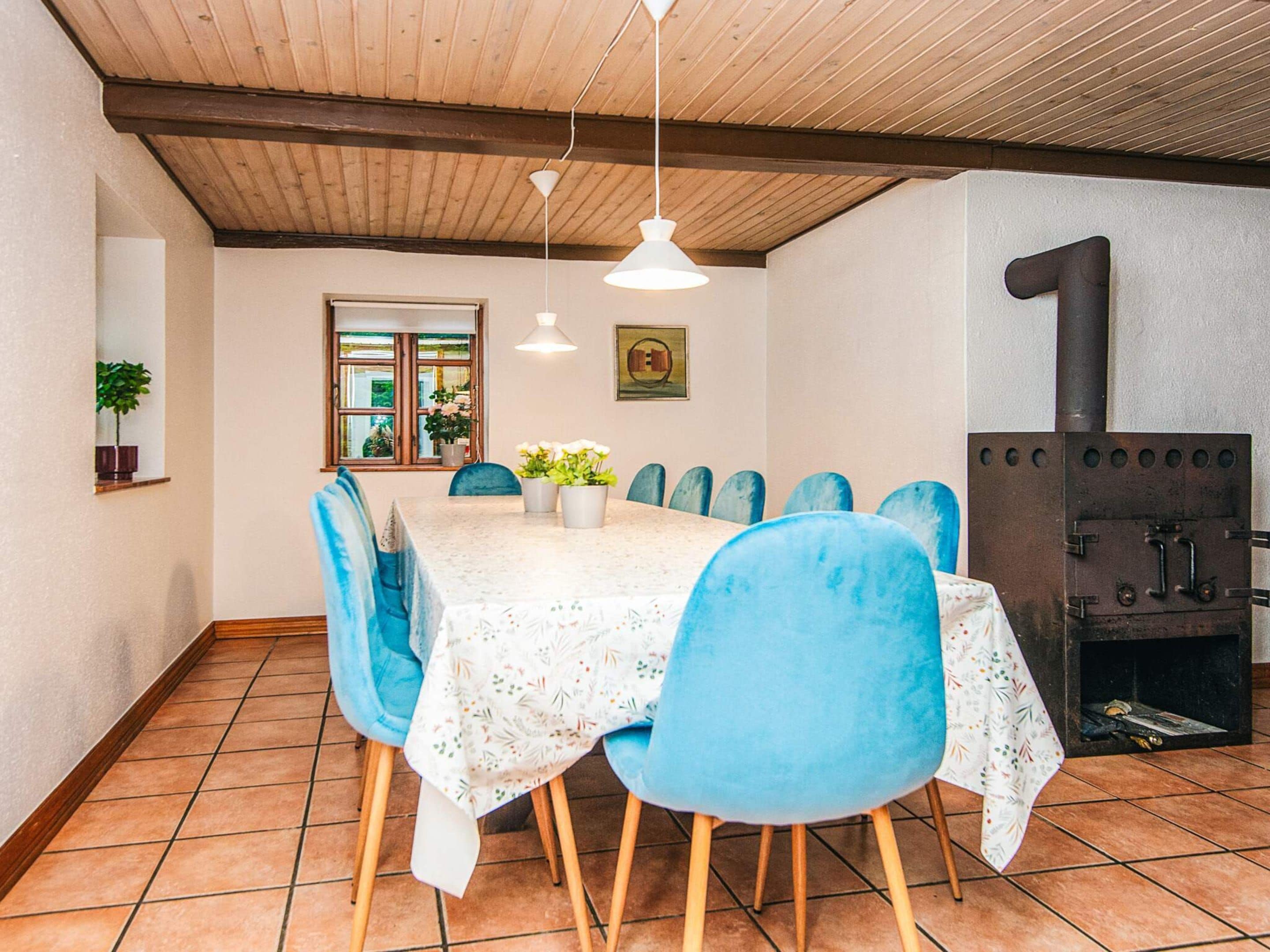 Un comedor con una mesa, sillas, lámpara colgante, ventana y estufa de leña.