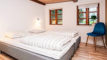A bedroom with a bed, two windows, a chair, and a lamp.