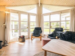 A room with a wooden floor, two leather chairs, a wooden table, and large windows with curtains. - 5 Star Holiday Home in Rodby (Rodby)