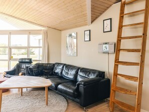 A modern living room with a black leather sofa, a wooden coffee table, and a wooden ladder against the wall. - 5 Star Holiday Home in Rodby (Rodby)