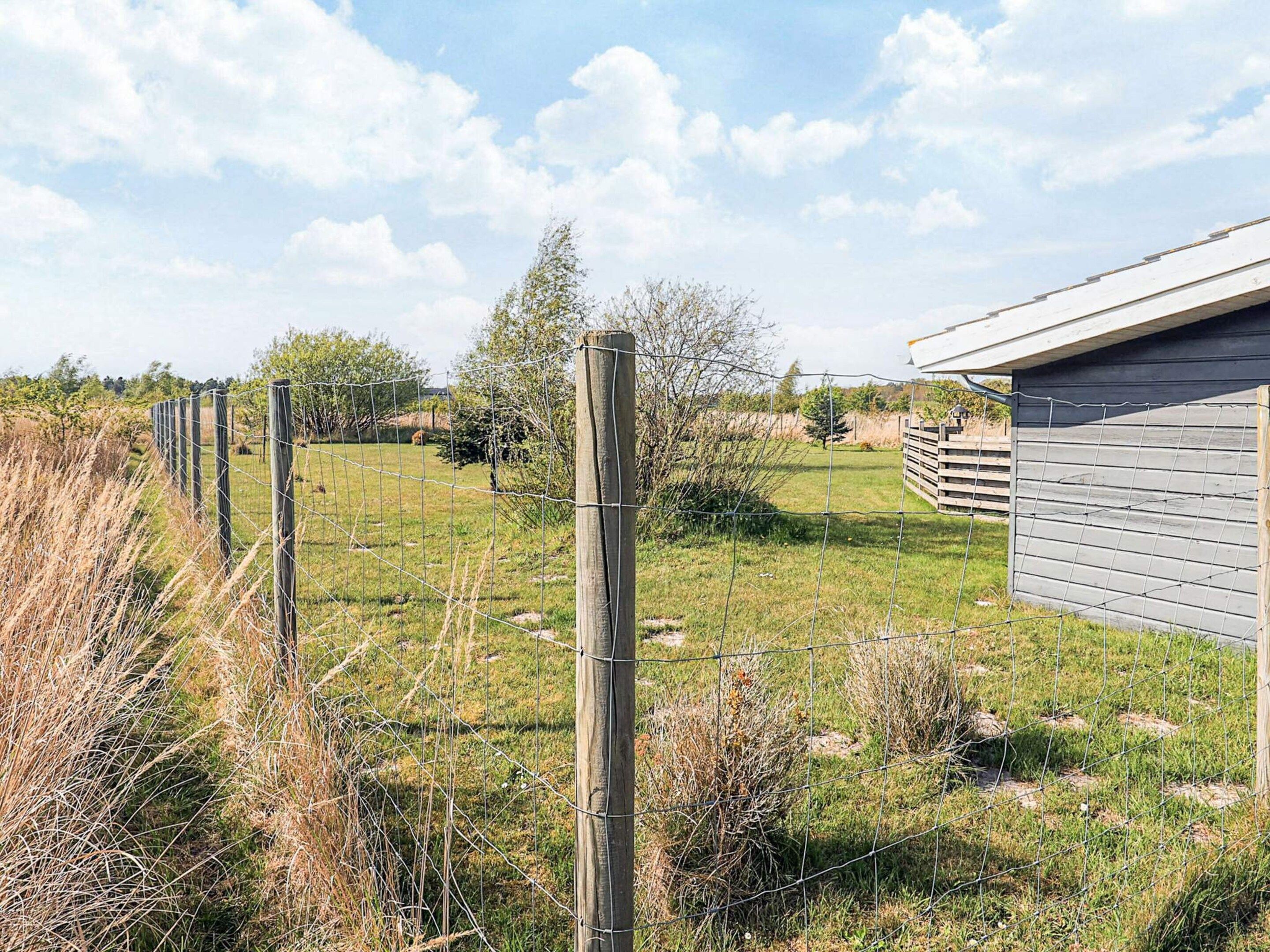 A fenced outdoor area with a building, likely a barn or storage shed, and a grassy field.