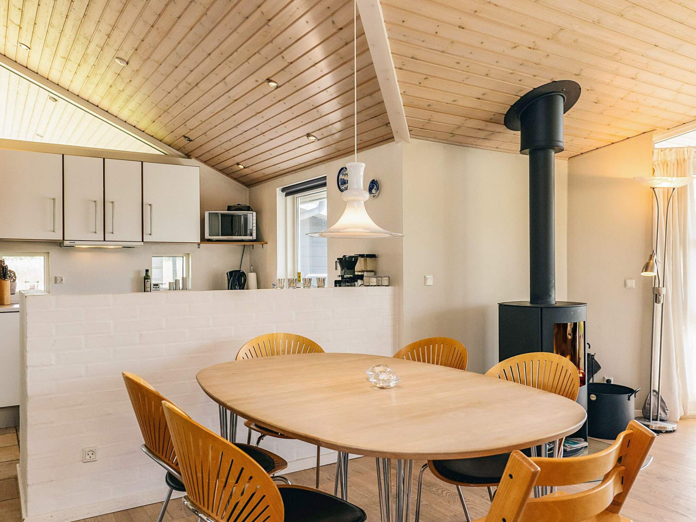 Eine moderne Küche mit weißen Schränken, einem runden Holztisch mit Stühlen, einem schwarzen Herd und einer hängenden Leuchte.