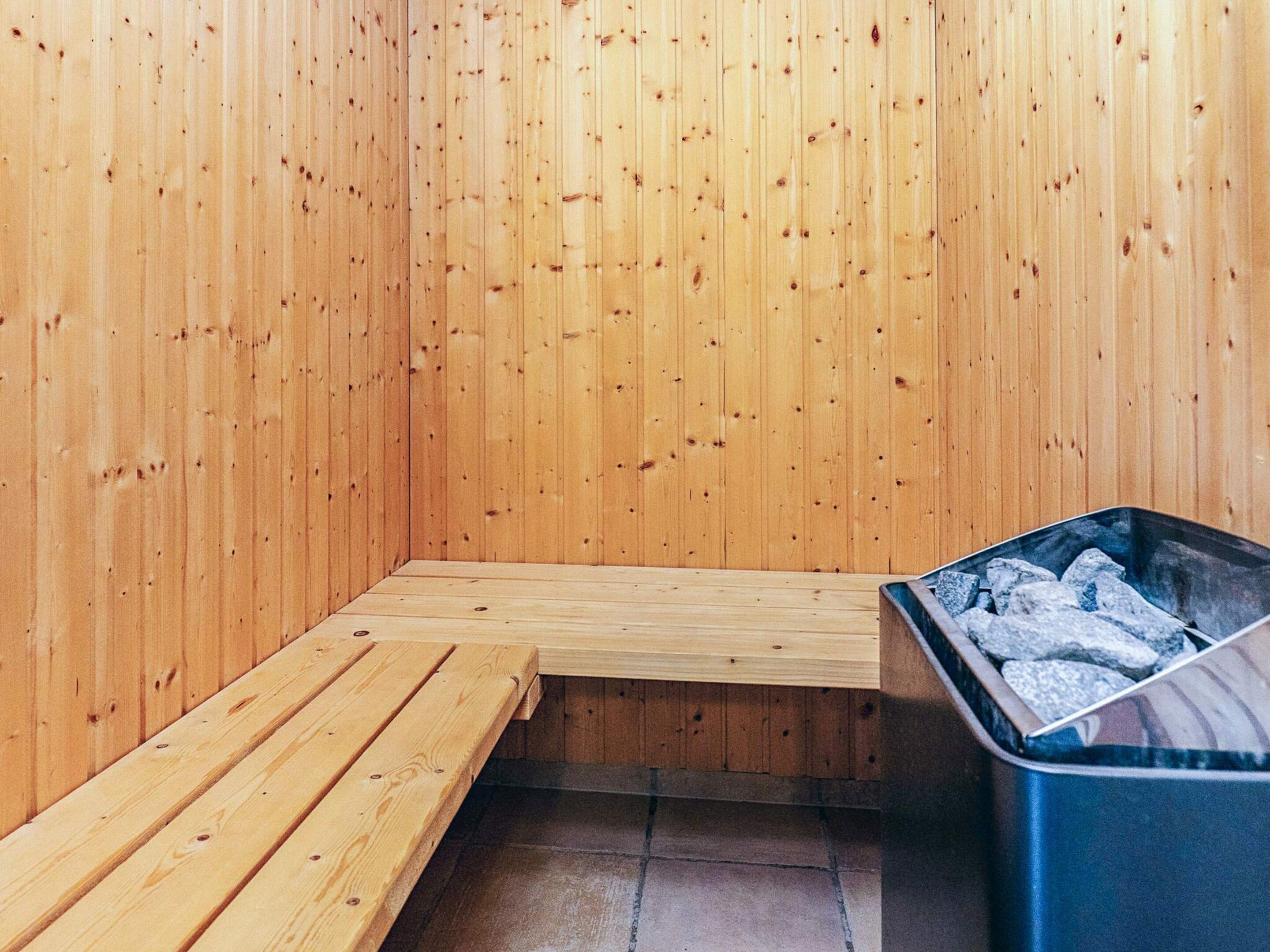 Eine Sauna mit Holzwänden und -bänken, gefliester Boden und ein Mülleimer mit Holzkohle.