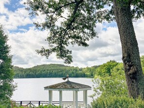 A gazebo by a lake with a view of a forested hill in the background. - 6 Person Holiday Home in Overum (Overum)