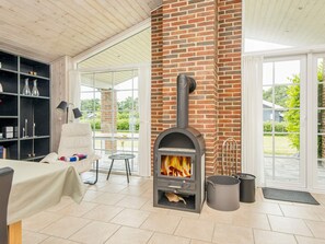 Una habitación con chimenea de ladrillo, un sillón blanco, una mesa con mantel y una estantería.
