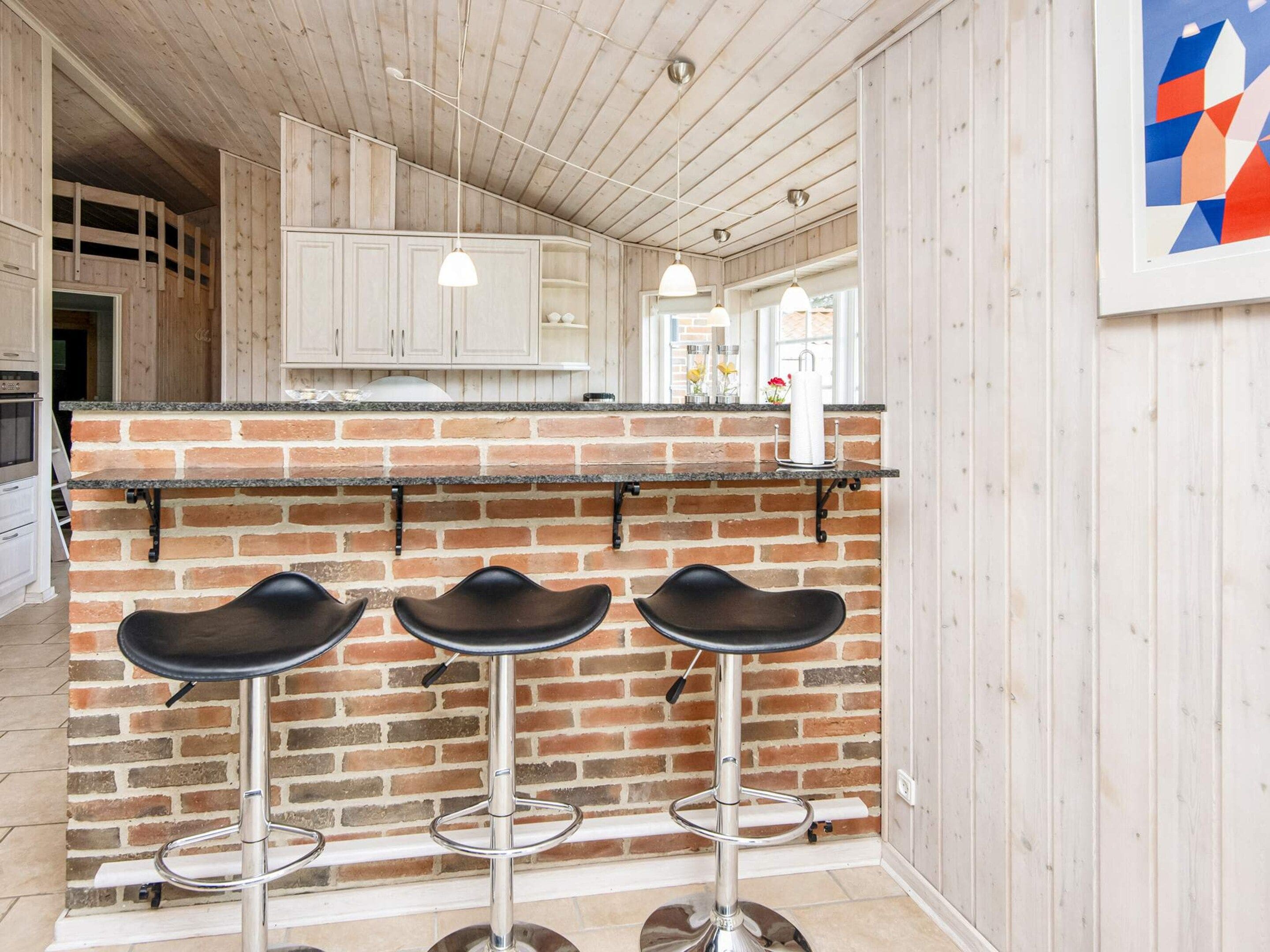 Een keuken met een tegelwand, witte kasten en een bar met drie krukken.