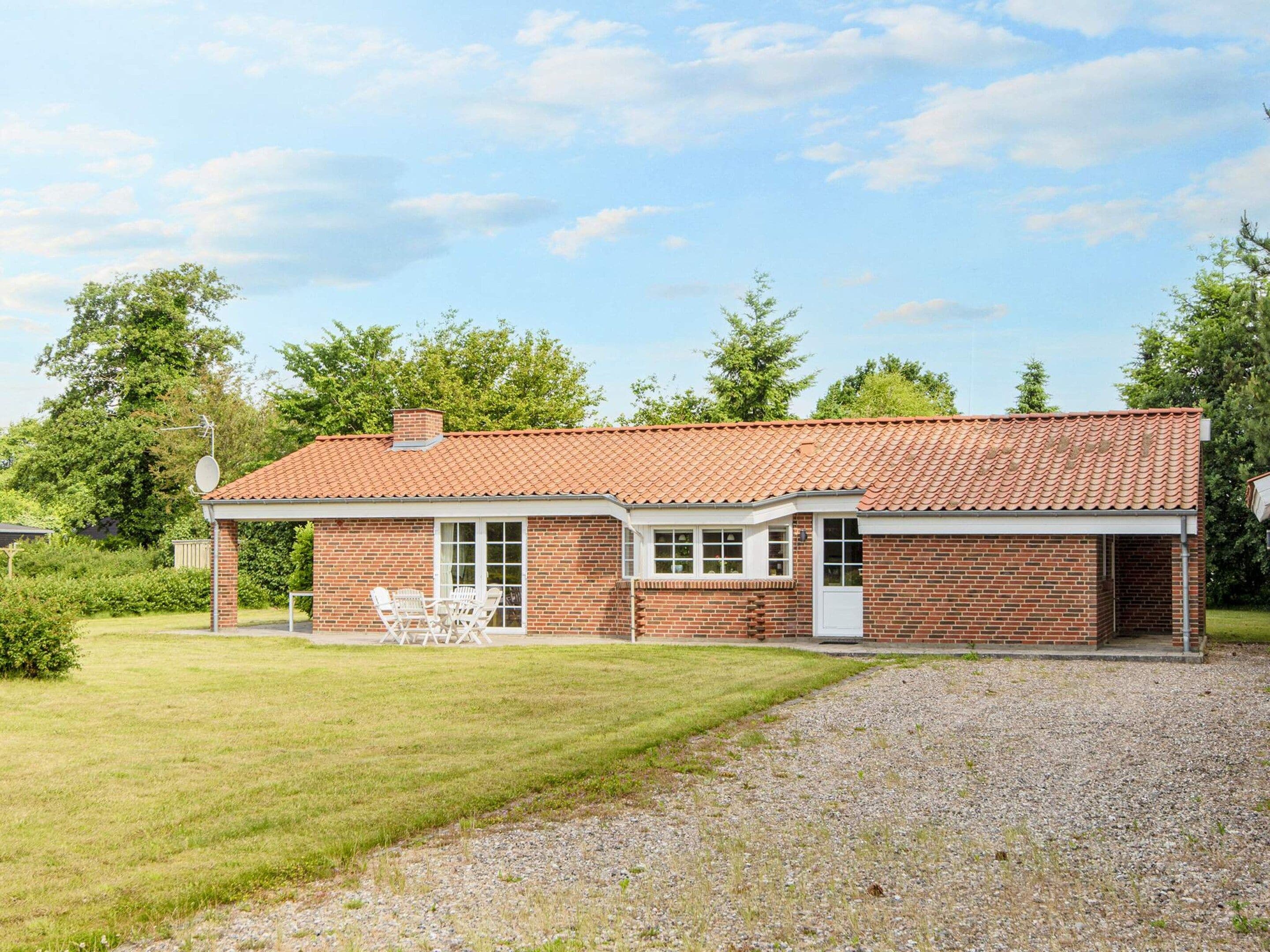 A single-story brick house with a red-tiled roof, a covered patio with outdoor furniture, and a gravel driveway.