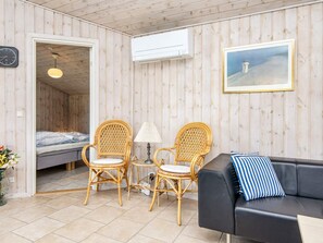 A room with a bed, two wicker chairs, a black sofa, a lamp, an air conditioning unit, and a framed picture on the wall. - 4 Star Holiday Home in Orsted (Ørsted)