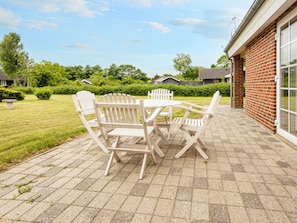 A patio with a table and chairs, a brick wall, and a grassy area with trees.