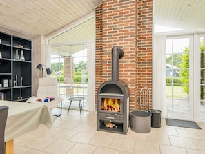 A room with a brick fireplace, a white chair, a table with a tablecloth, and a bookshelf. - 4 Star Holiday Home in Orsted (Ørsted)