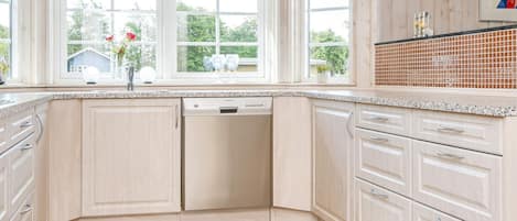 A kitchen with light wood cabinets, a dishwasher, and a tiled backsplash.