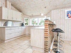 A kitchen with wooden cabinets, a brick accent wall, a coffee machine, and a bar stool. - 4 Star Holiday Home in Orsted (Ørsted)