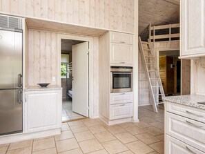 A kitchen with white cabinetry, a stainless steel refrigerator, a built-in oven, and a wooden ladder. - 4 Star Holiday Home in Orsted (Ørsted)