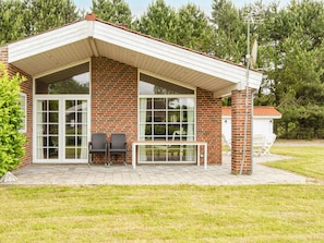 Una casa de dos pisos con fachada de ladrillo, ventanas grandes y un porche cubierto con mobiliario exterior.