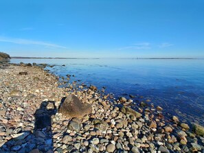 A pebbled beach with clear water and distant land.