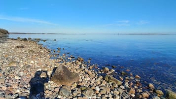 A pebbled beach with clear water and distant land.