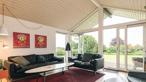 A modern living room with a black leather sofa, a white coffee table, and a red rug. There are two large windows providing a view of the outdoors. - 5 Star Holiday Home in Faaborg (Faaborg)
