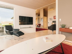 Un salon moderne avec un téléviseur à écran plat, des fauteuils en cuir noir, une table basse blanche et un tapis rouge.