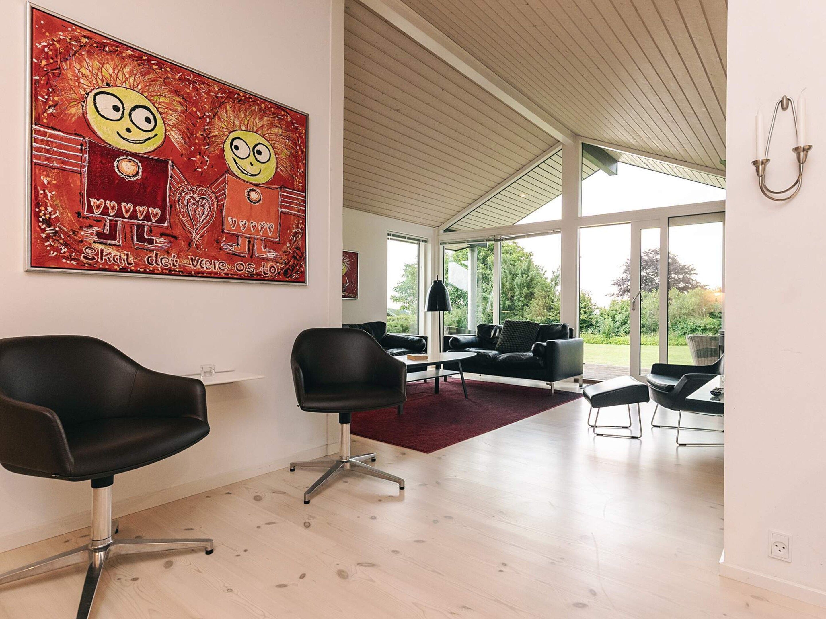 A spacious room with a large window, a black leather chair, a black sofa, and a red abstract painting on the wall.