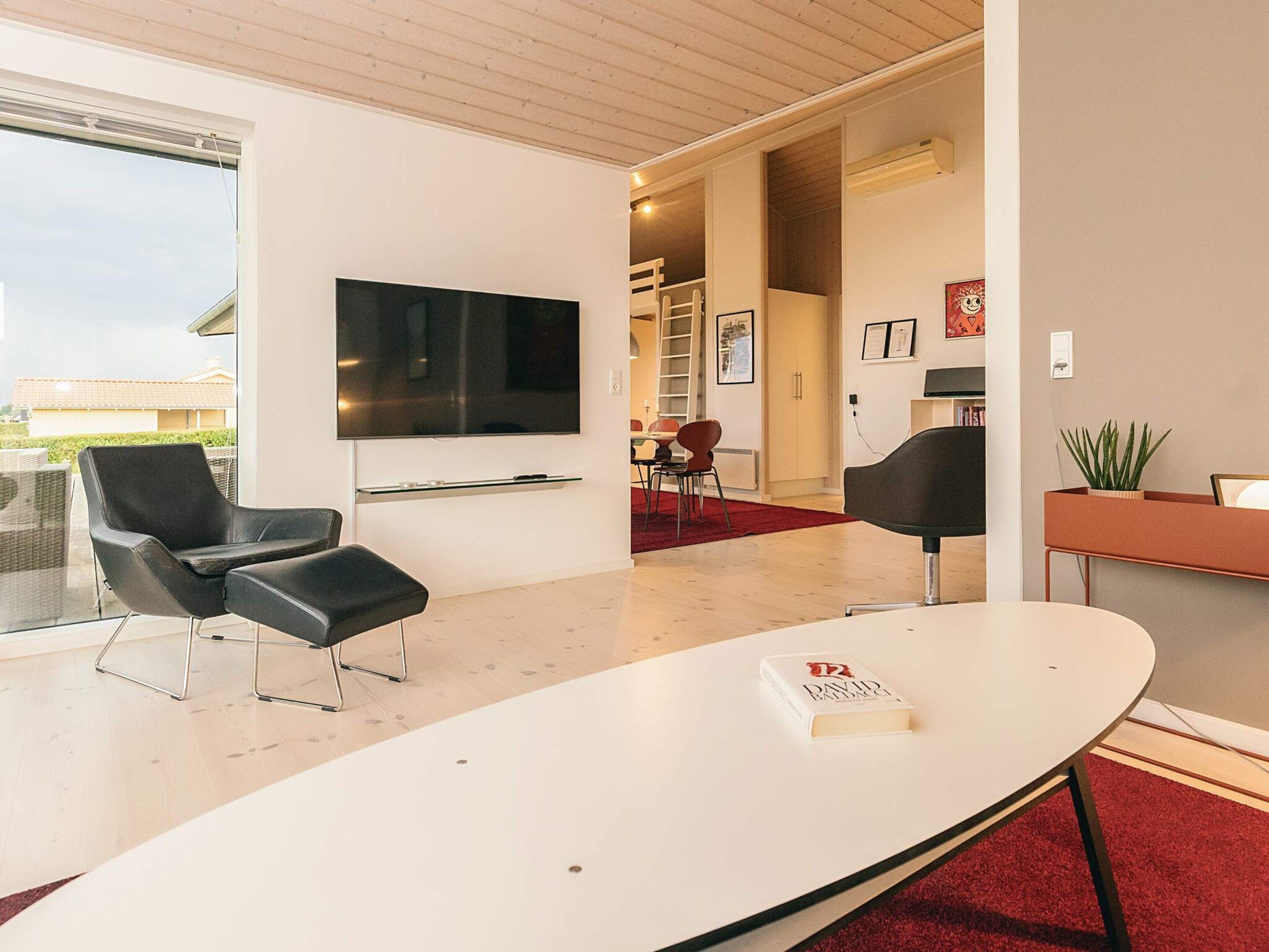 Un salon moderne doté d’un téléviseur à écran plat, d’un coin repas avec des chaises et d’un tapis rouge.
