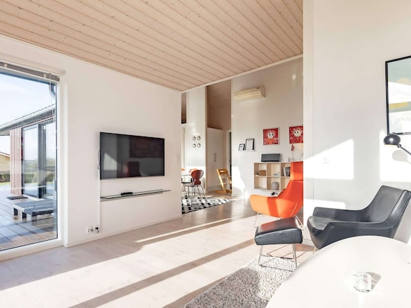 A modern living room with a flat-screen TV, a dining area with a table and chairs, and a large window providing natural light. - 5 Star Holiday Home in Faaborg (Faaborg)