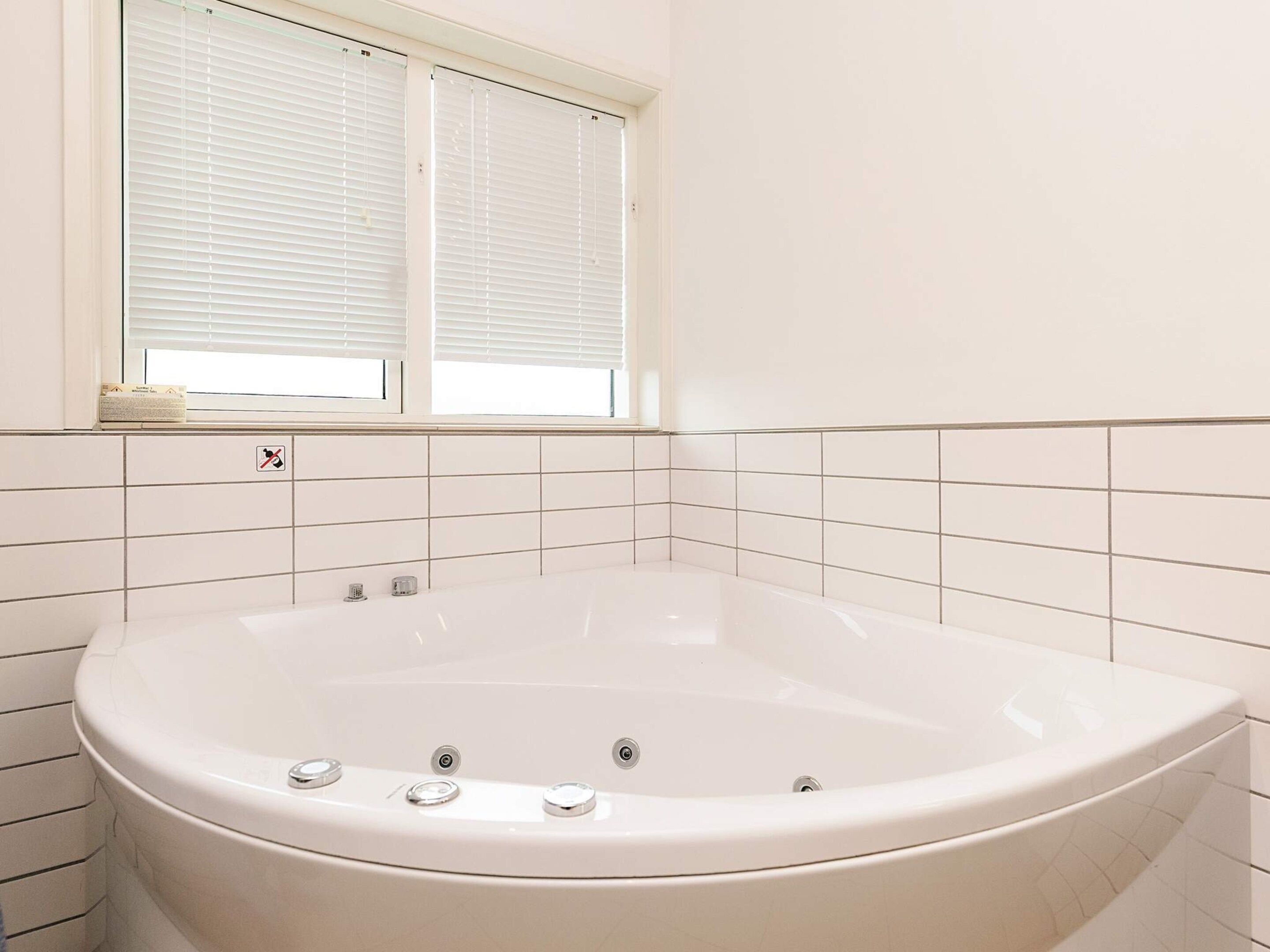 A bathroom with a freestanding bathtub, a window with blinds, and a no-smoking sign.