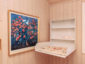 Een kamer met houten lambrisering, een lijst met rode bloemen en een wit wandrek met een kussen.
