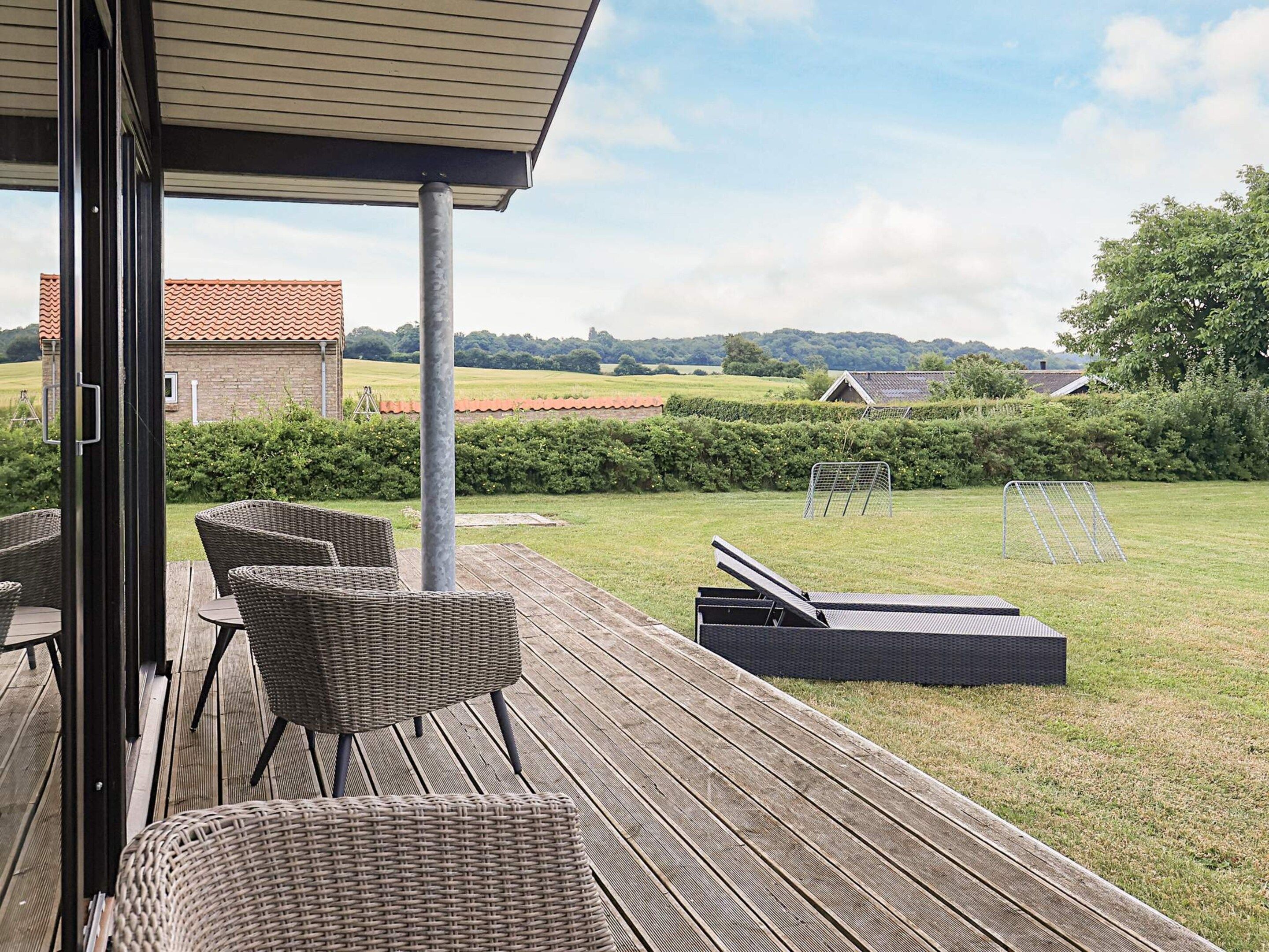 A covered outdoor deck with wicker furniture, a metal table, and a view of a grassy field with a building in the background.