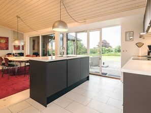 Une cuisine moderne dotée d’un îlot central, de grandes fenêtres et d’un coin repas avec des chaises.