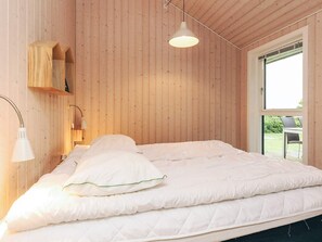 A bedroom with a wooden wall, a bed with white bedding, a hanging lamp, and a window with a view of the outdoors. - 5 Star Holiday Home in Faaborg (Faaborg)