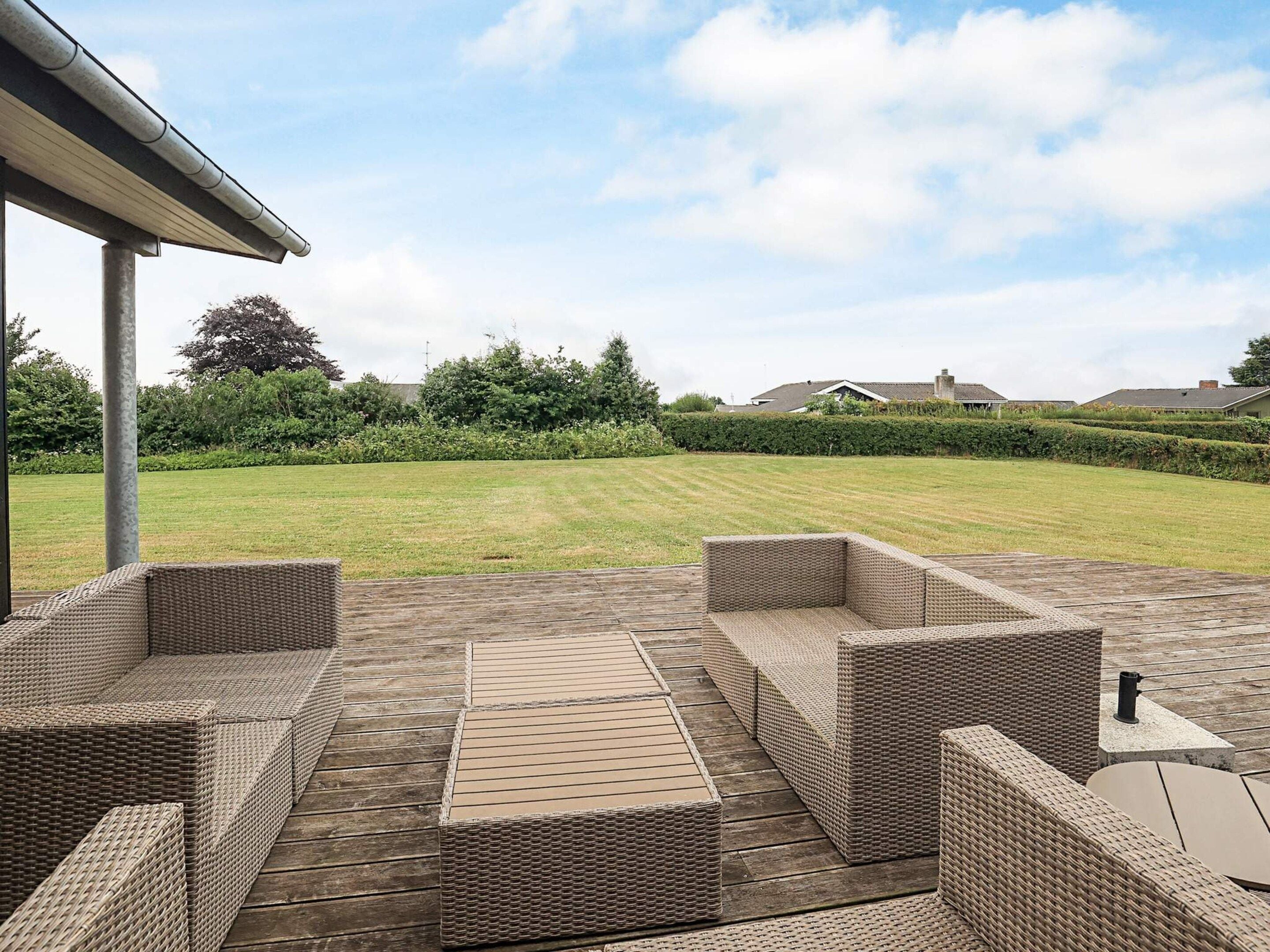 Een overdekt terras met rieten meubels en een houten dek.
