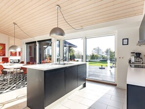 A modern kitchen with a large island, a dining area with orange chairs, and a view of the outdoors.