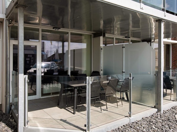 A modern outdoor seating area with glass partitions and metal furniture.