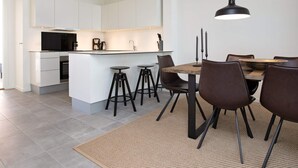 A modern kitchen with white cabinetry, a central island with stools, and a dining area with a wooden table and chairs. - Spacious Apartment in RingkÃ¸bing near Sea (Ringkobing)