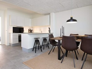 A modern kitchen with white cabinetry, a central island with stools, and a dining area with a wooden table and chairs. - Spacious Apartment in RingkÃ¸bing near Sea (Ringkobing)