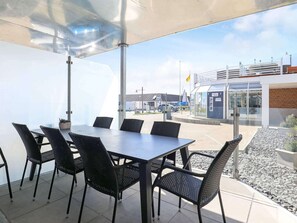 An outdoor patio with a table and chairs, a covered area, and a view of a building with a glass facade and a flag.