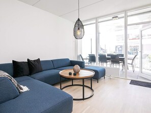 A modern living room with a sectional sofa, a round coffee table, and a hanging light fixture. - Spacious Apartment in RingkÃ¸bing near Sea (Ringkobing)